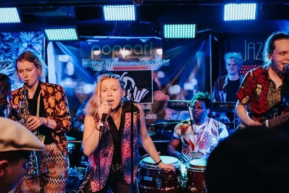 A live band with saxophone, vocals and percussion performs on stage