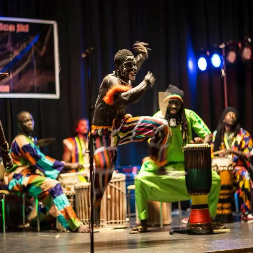 A dancer leaps in front of drummers in bright traditional outfits