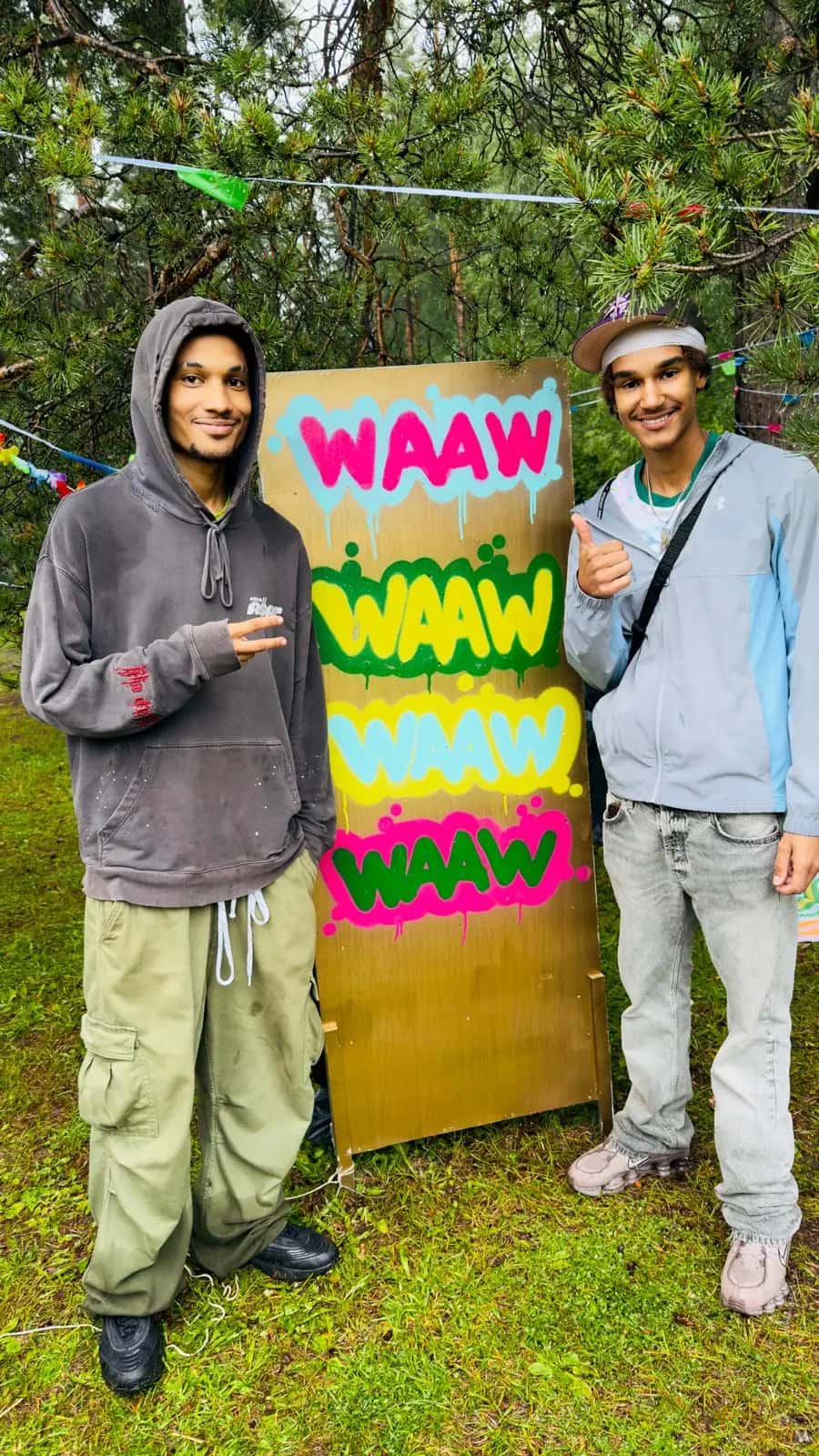 Two young artists pose beside a freshly painted WAAW graffiti board