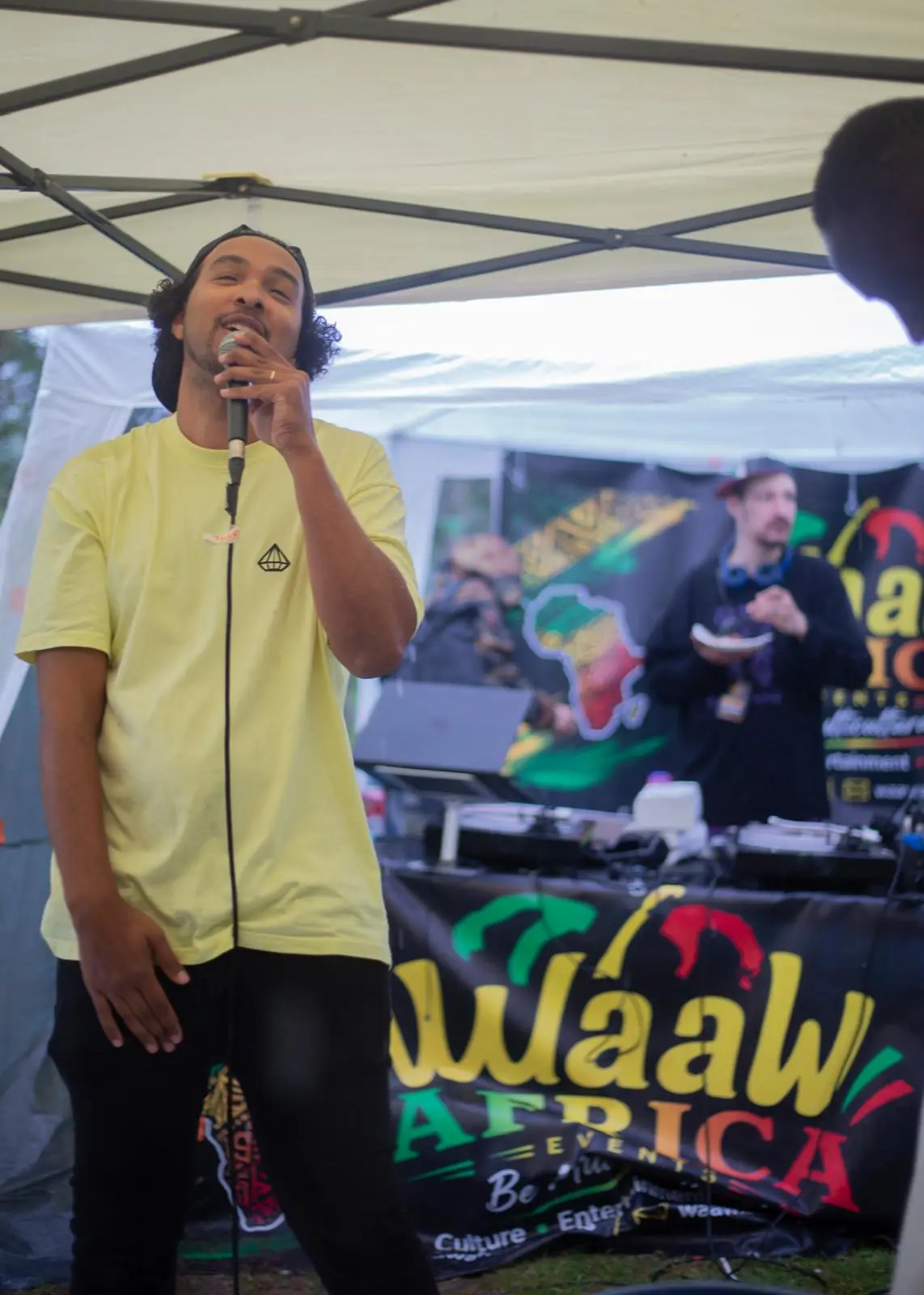 An MC in a yellow shirt performs in front of the WaawAfrica banner