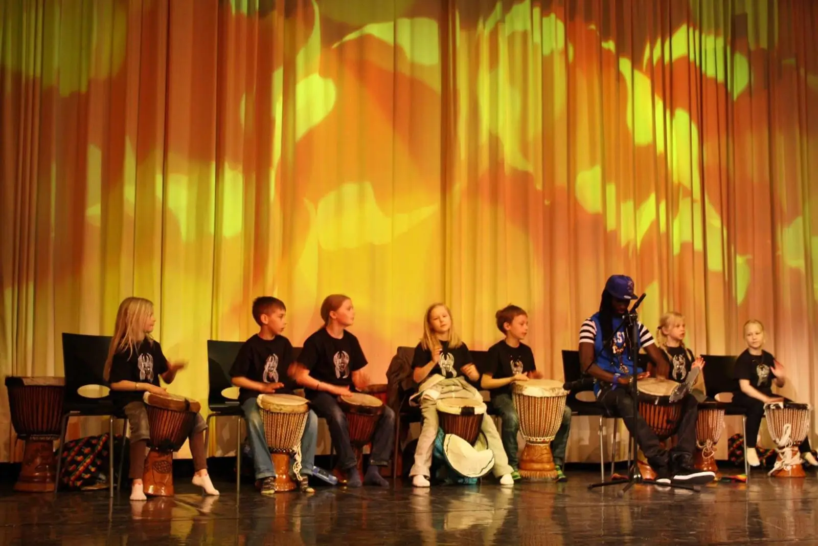 Schoolchildren learn to play djembe drums on stage